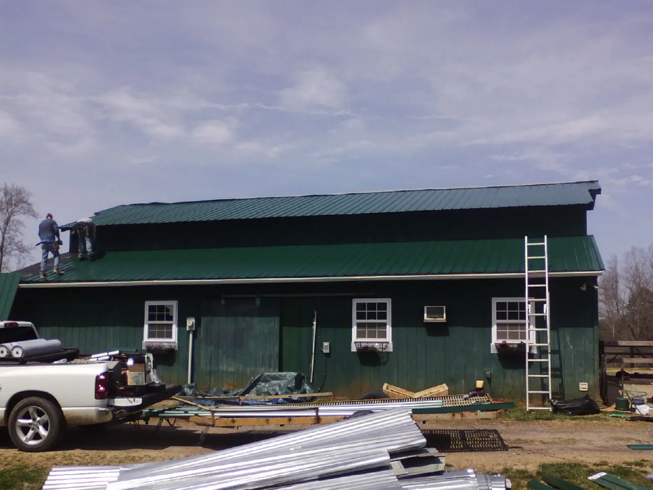 Crew installing green metal roofing on a large green barn in Dawson