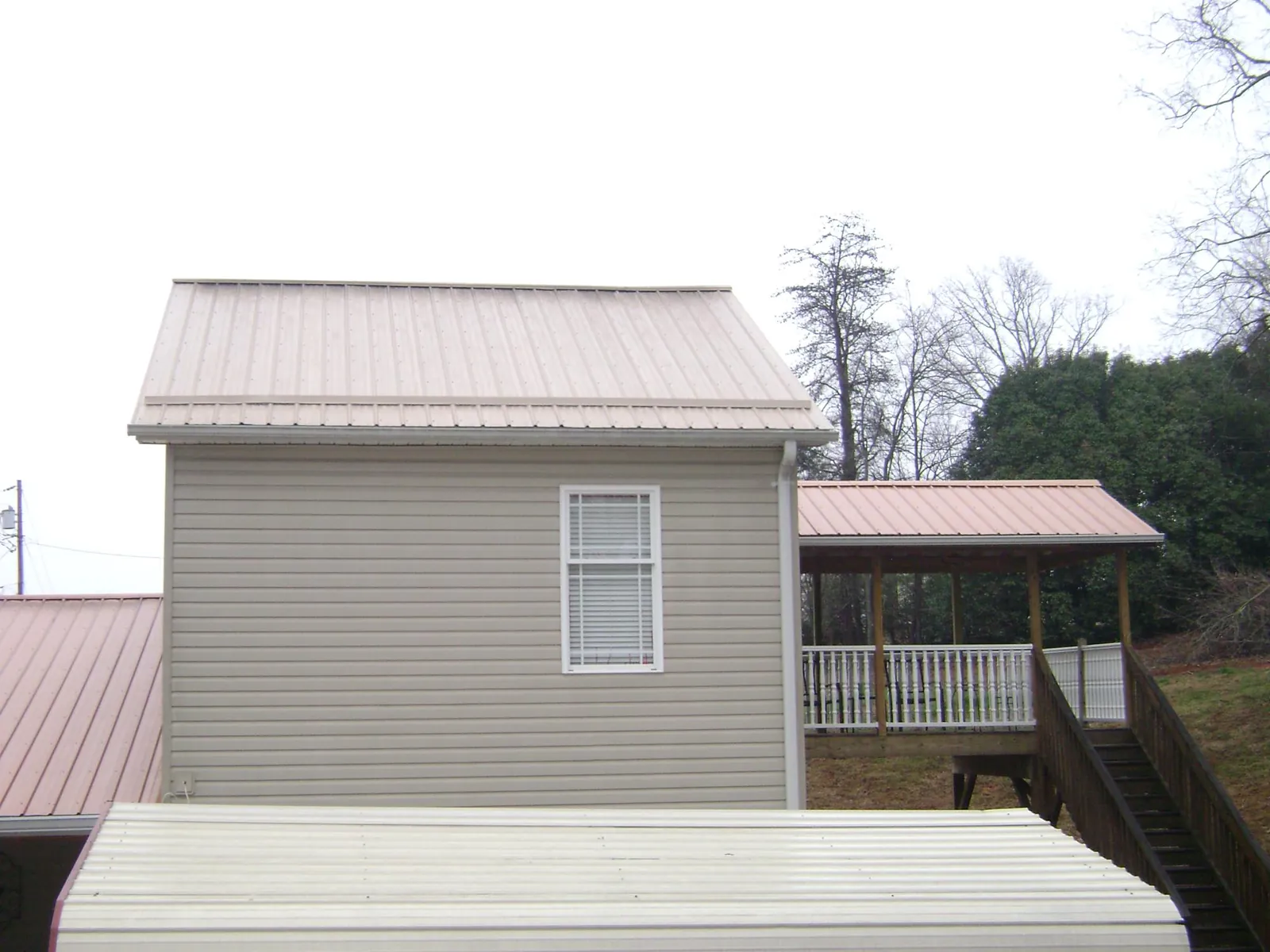 Tan metal roofs on a two story addition and attached porch, from a Roof Replacement job in Dawson